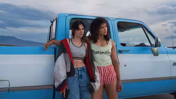 Lou (Kristen Stewart) with her arm around Jackie (Katy O'Brian) beside a blue truck