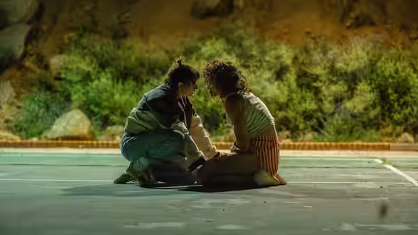 Lou (Kristen Stewart) kneeling before Jackie (Katy O'Brian) on an empty road at night