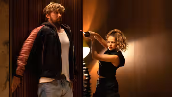 Colt Seavers (Ryan Gosling) stands against a wall as a woman aims a gun
