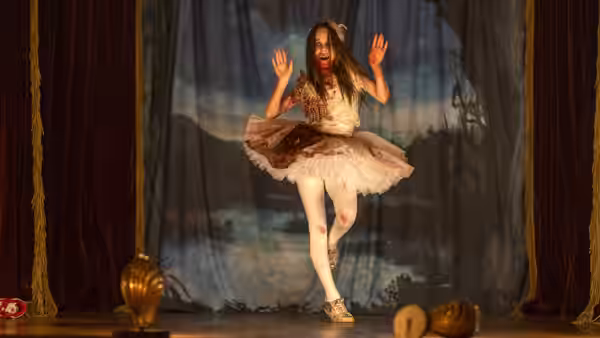 Abigail (Alisha Weir) stands on stage with hands raised, covered in blood