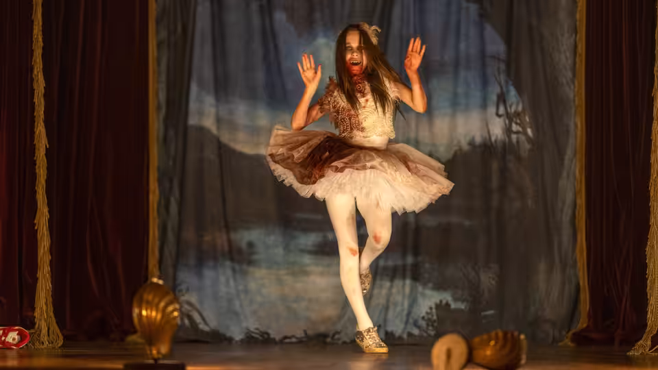 Abigail (Alisha Weir) stands on stage with hands raised, covered in blood