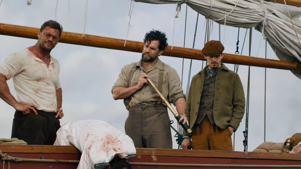 Three men stand over a bloodied body on a wooden ship deck
