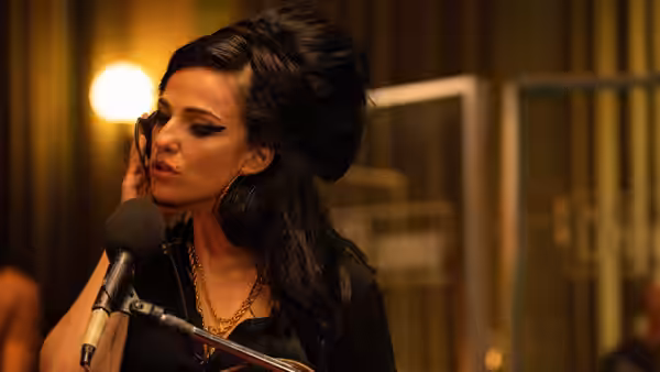 Amy (Marisa Abela) singing into a studio microphone with hand to cheek