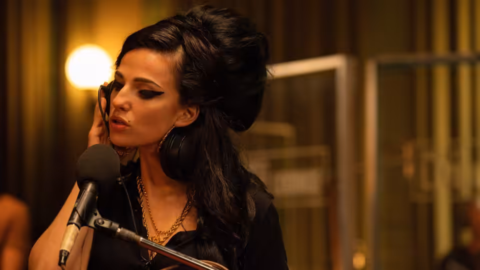 Amy (Marisa Abela) singing into a studio microphone with hand to cheek