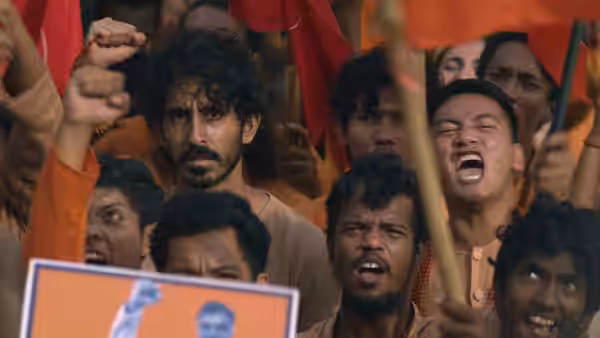Kid (Dev Patel) in a crowd of shouting protesters with flags