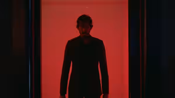 Kid (Dev Patel) stands in a black suit in a red-lit doorway