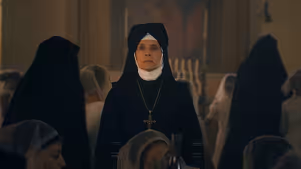 an older nun wearing a crucifix necklace stands among other veiled women in a church