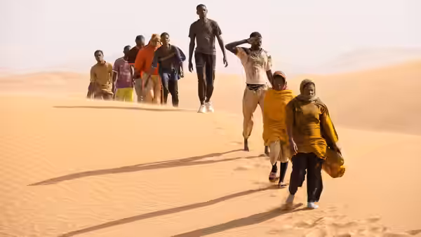 group of people walking through sand dunes in daylight