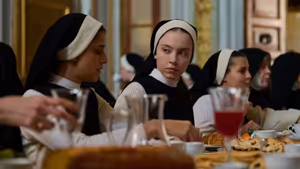 Nuns in habits sit at a long dining table during a meal in a hall