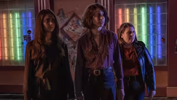 Jamie, Marian and Sukie standing together in a room with colorful windows