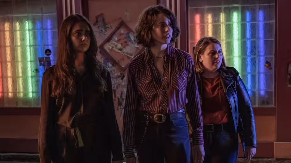 Jamie, Marian and Sukie standing together in a room with colorful windows