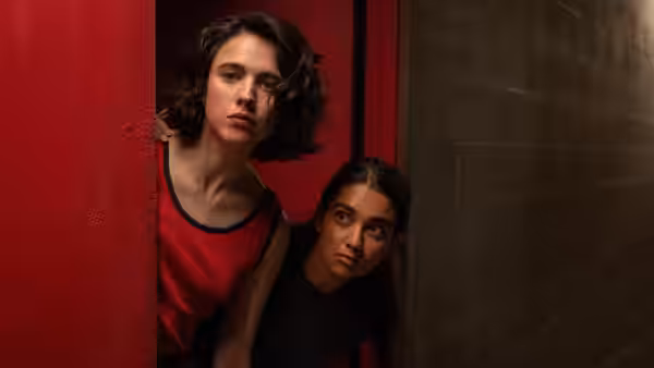 Jamie and Marian looking out from behind a red door at night