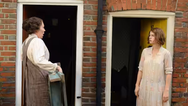 Two women conversing from the doorways of neighboring houses on a brick street