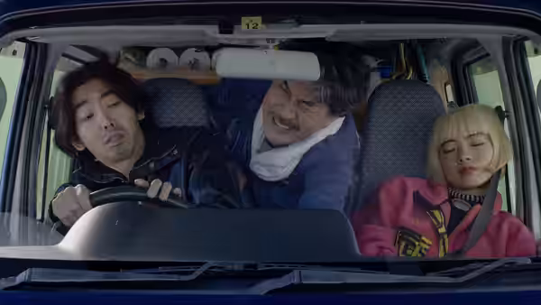 Hirayama (Koji Yakusho) leans forward in a van between a driver and a young woman