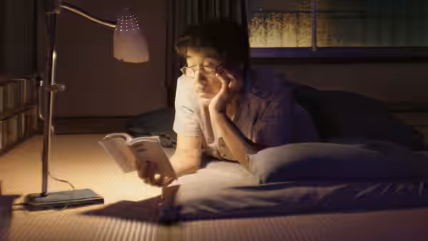Hirayama (Koji Yakusho) lies on a bed reading a book under a lamp at night