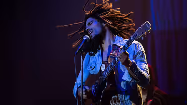 Bob Marley (Kingsley Ben-Adir) singing and playing guitar on stage at microphone
