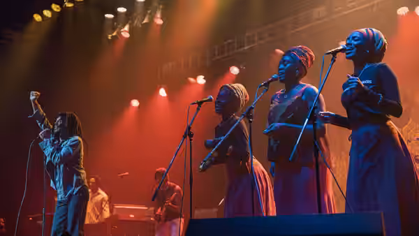 Bob Marley (Kingsley Ben-Adir) and female vocalists performing together on brightly lit stage