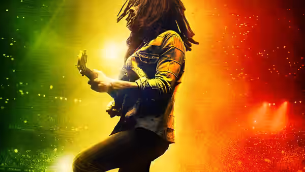 Bob Marley (Kingsley Ben-Adir) playing guitar on stage with yellow and red lights