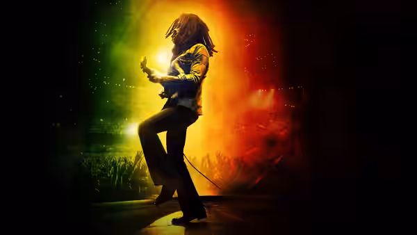 Bob Marley (Kingsley Ben-Adir) playing guitar on stage with crowd visible behind