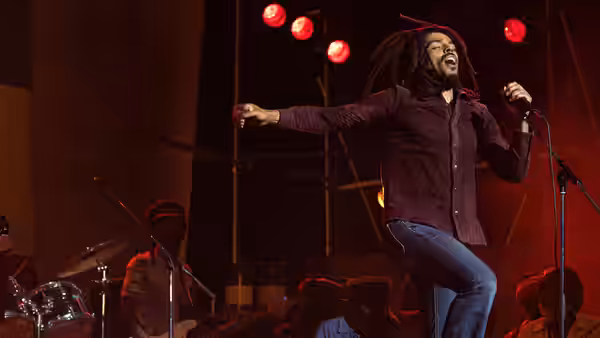 Bob Marley (Kingsley Ben-Adir) singing with arms extended on stage under red lights