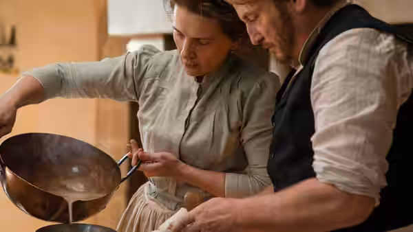 Eugénie (Juliette Binoche) pouring sauce from a pan while Dodin watches in the kitchen