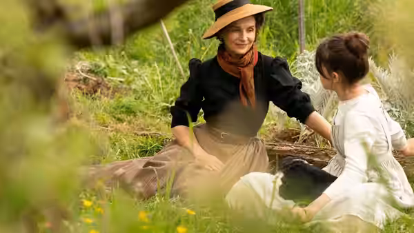Woman in a hat sitting with a young woman in a meadow among wildflowers