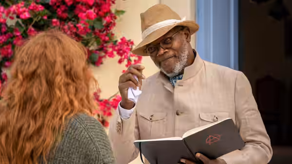 Alfie (Samuel L. Jackson) holds an open book while speaking to a red-haired woman