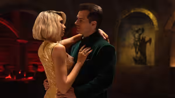 A blonde woman in a gold dress dances closely with a man in a green velvet jacket