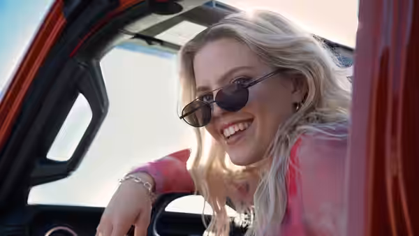 Regina George (Reneé Rapp) smiles from the open door of a red car