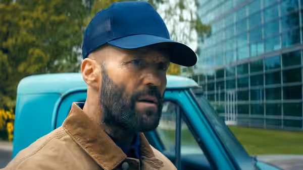 Adam Clay (Jason Statham) in a blue cap beside a turquoise truck