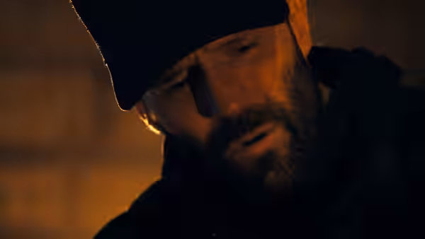 Adam Clay (Jason Statham) in a black cap looking down with intense focus