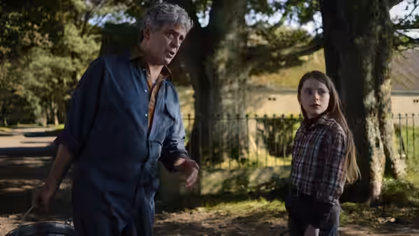 Seán (Andrew Bennett) and Cáit (Catherine Clinch) stand together beneath trees by a garden gate