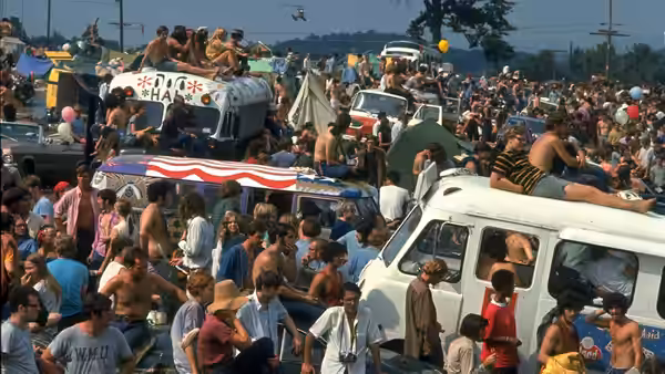 Dense crowd of people gathered around vans and tents in a field