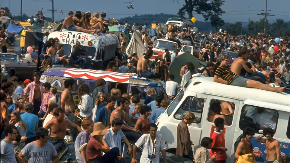 Dense crowd of people gathered around vans and tents in a field
