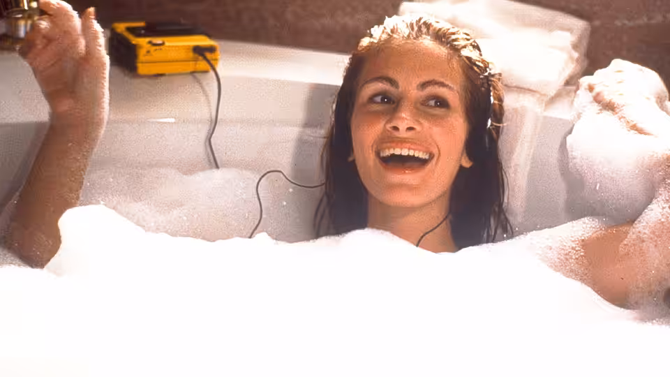 Vivian Ward (Julia Roberts) laughing in a bubble bath with headphones on