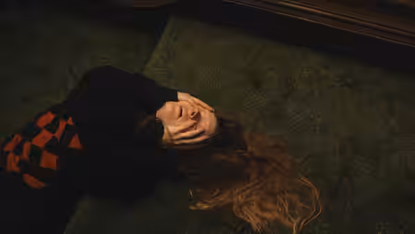 Maud (Morfydd Clark) lies on the floor with her hands covering her face