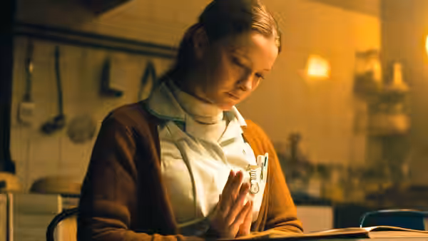 Maud (Morfydd Clark), wearing her nurse uniform, clasps her hands in prayer