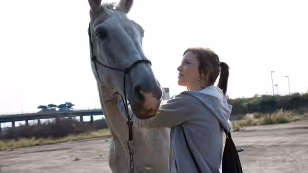 Mia (Katie Jarvis) reaching up to touch a white horse's face