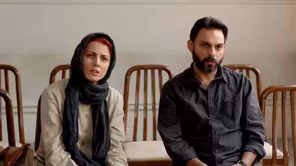 A woman in a headscarf sits beside a bearded man on wooden chairs in a hall