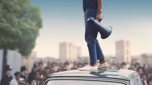 Man standing on a car roof holding a megaphone above a crowd