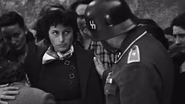 A German soldier questions a woman while a crowd looks on
