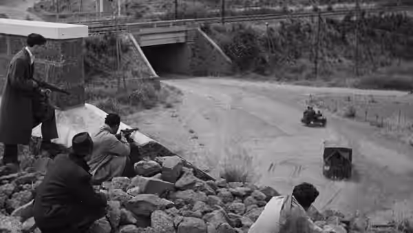 Armed men take cover behind rocks and aim at a passing vehicle