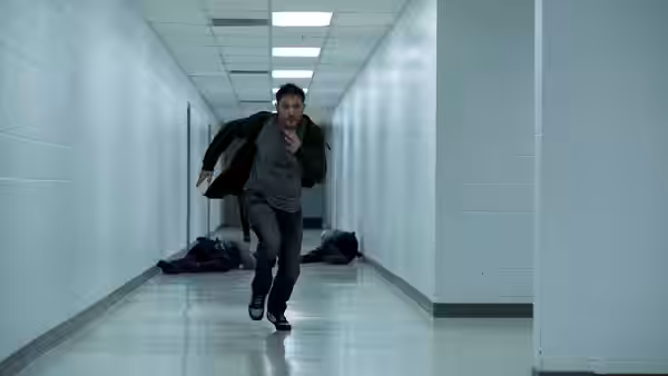 Eddie Brock (Tom Hardy) runs down a white hallway past fallen guards