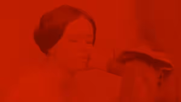a dark-haired woman lies with eyes closed under red lighting