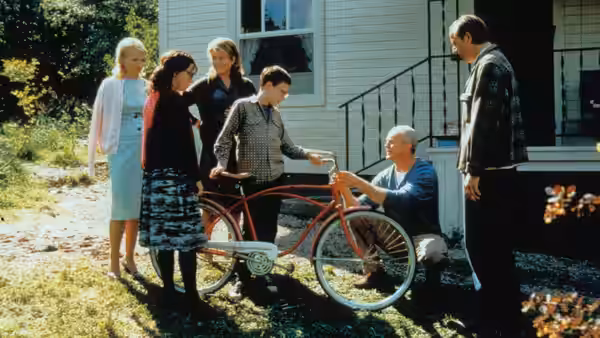 Family gathered around a red bicycle outside a white house