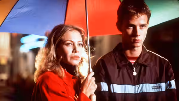 Manuela holds an umbrella beside a young man on a city street