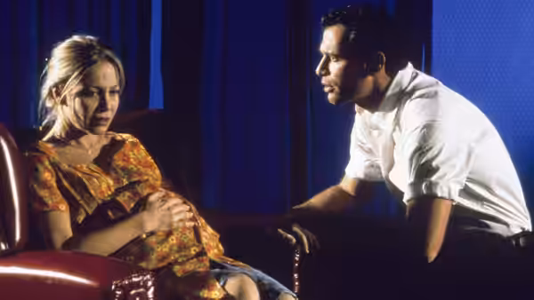 A seated pregnant woman talks with a man in a blue-curtained room