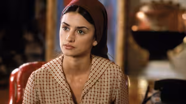 Rosa sits at a table wearing a headscarf and patterned cardigan