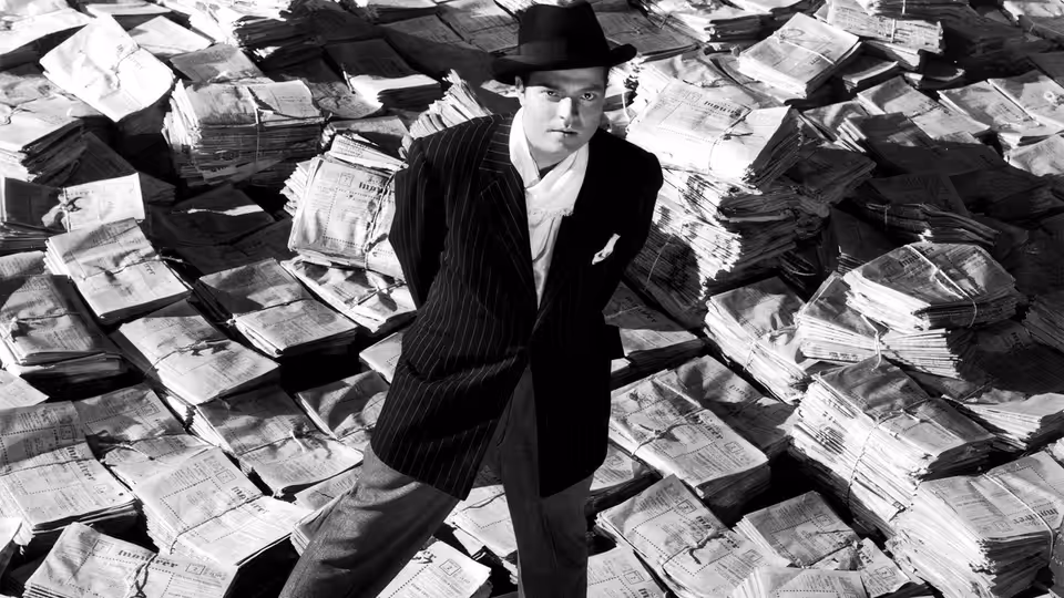 Charles Foster Kane (Orson Welles) standing on stacks of newspapers