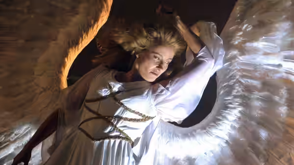 a blonde winged woman in white looks down with arm raised